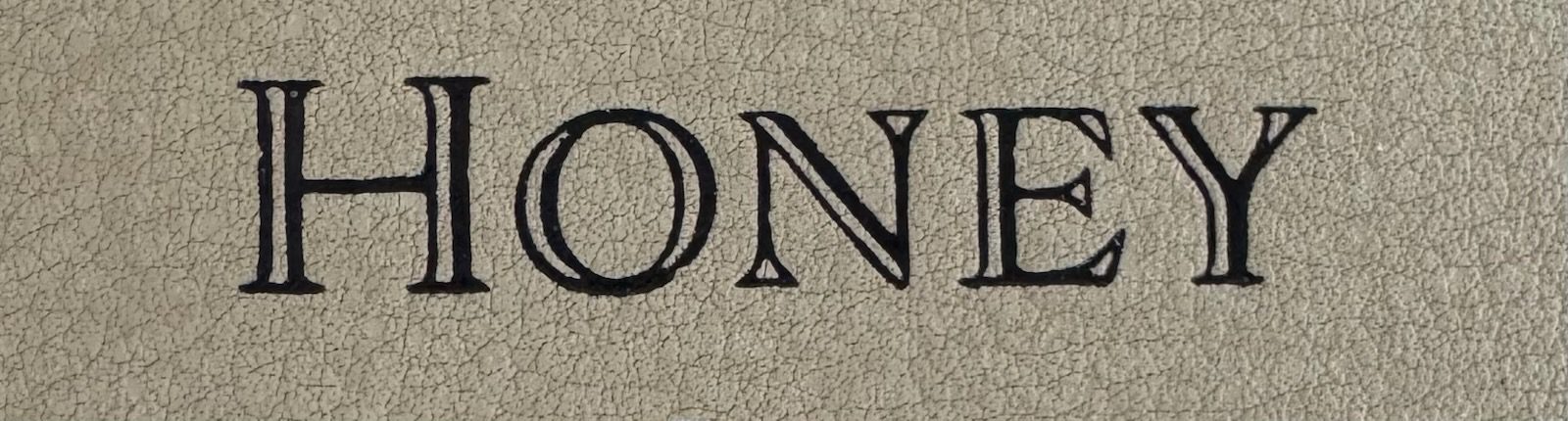 Black serif lettering spelling 'HONEY' on beige